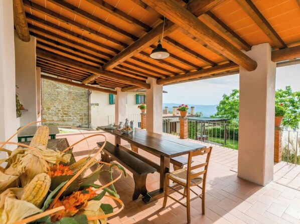 An outdoor patio with a wooden table and chairs, a stone wall, and a view of the sea.