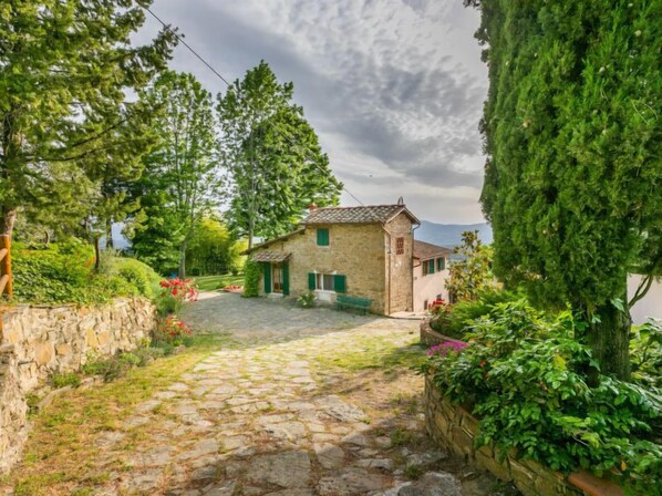A stone house with a stone pathway leading to it, surrounded by greenery and trees. - Podere Berrettino by Interhome (Reggello)