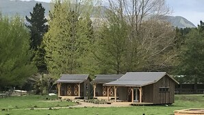A rustic cabin with a large porch and a barn in a rural setting with mountains in the background. - Mohaka River Farm - Campsite (Te Haroto)