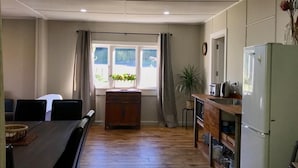 A compact kitchen with a refrigerator, wooden cabinets, and a dining table with chairs. - Mohaka River Farm - Campsite (Te Haroto)