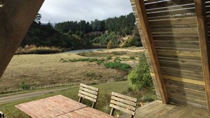 A wooden deck with a table and chairs overlooking a natural landscape with a river and forested hills. - Mohaka River Farm - Campsite (Te Haroto)