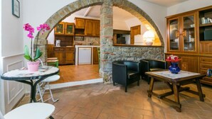 A cozy living area with a stone archway leading to a kitchen, featuring wooden cabinets and a dining table with chairs. - Appartamento Piccolo by Interhome (Reggello)