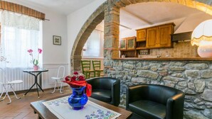 A cozy room with a stone wall, a wooden cabinet, a blue vase, and a table with a floral tablecloth. - Appartamento Piccolo by Interhome (Reggello)