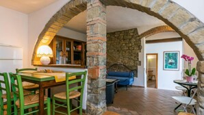 A dining area with a stone archway, a wooden table, and green chairs. - Appartamento Piccolo by Interhome (Reggello)