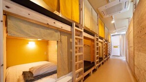 A row of bunk beds in a narrow hallway with wooden walls and a light fixture above the beds. - Million Pointz - Hostel (Amami)