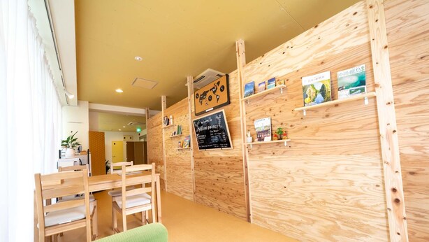 A wooden interior with a reception desk, a green couch, and shelves with books and maps. - Million Pointz - Hostel (Amami)