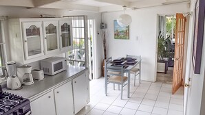 A kitchen with white cabinets, a microwave, and a gas stove. There is a dining area with a table and chairs. - View 61 Hibiscus with Private pool & Beach View (St John's)