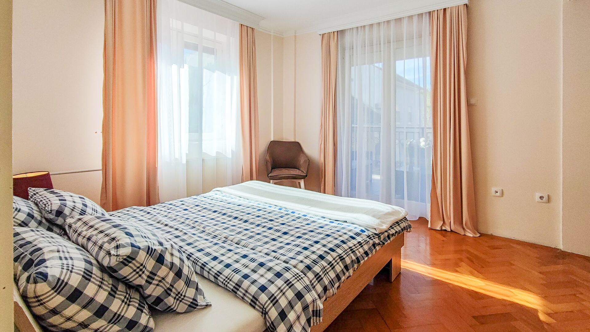 Een slaapkamer met een bed, een stoel en grote ramen met dunne gordijnen.