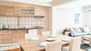 Une cuisine moderne avec des meubles en bois, une table à manger pour quatre personnes et un coin salon avec un canapé et un tableau au mur.