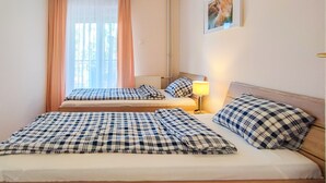 Une chambre avec deux lits, chacun recouvert d’une couverture à carreaux et agrémenté d’oreillers, une lampe de chevet et une fenêtre avec des rideaux.