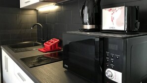 Una cocina compacta con microondas, cafetera y un recipiente rojo en la encimera.