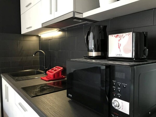 Una cocina compacta con microondas, cafetera y un recipiente rojo en la encimera.