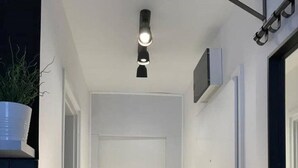 Un pasillo estrecho con una puerta blanca al final, un felpudo pequeño en la entrada y una lámpara en el techo.