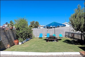 Relax in an outdoor space surrounded by lush greenery and a shaded patio area with a picnic table and lounge chairs.