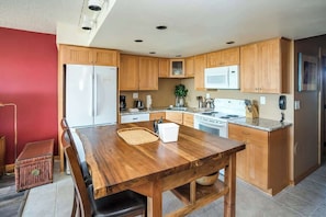 A compact kitchen with wooden cabinets, a stainless steel refrigerator, a microwave, and a dining table with chairs.