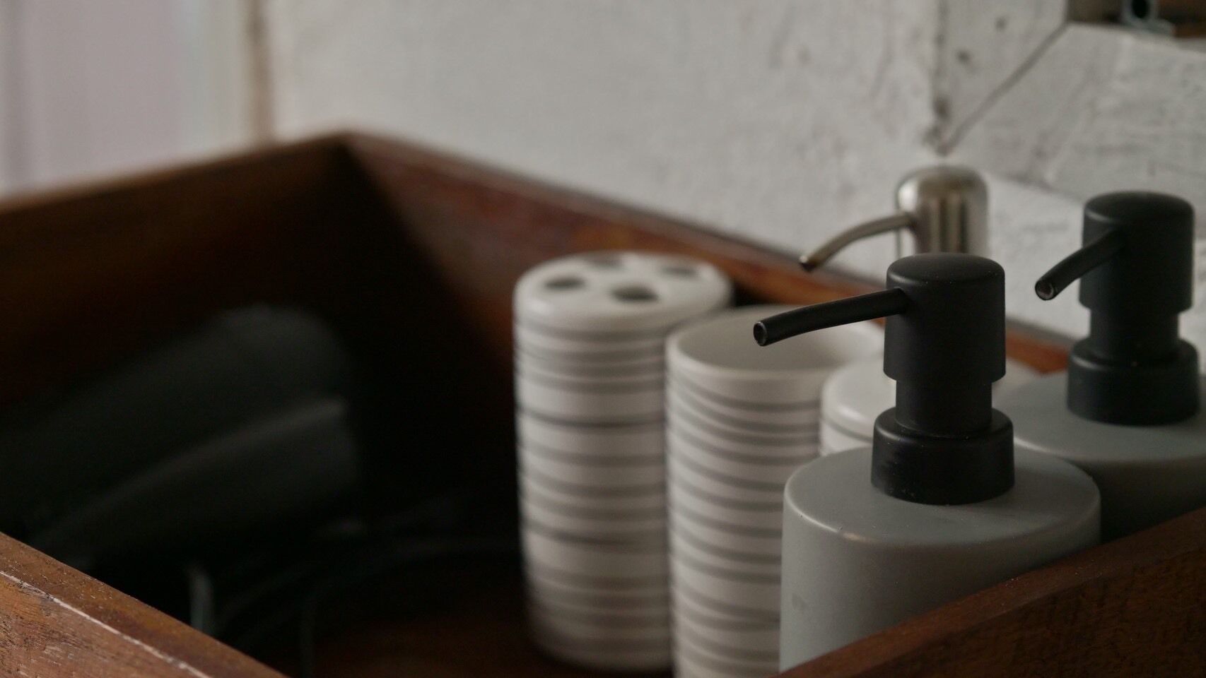 Un recipiente de madera con un objeto negro y dos contenedores cilíndricos blancos con dispensadores negros.