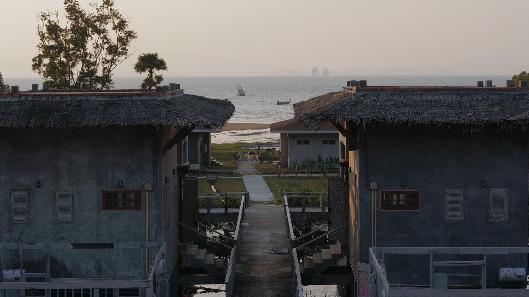 Un camino que lleva a una playa con edificios de techo de paja y vistas al mar.