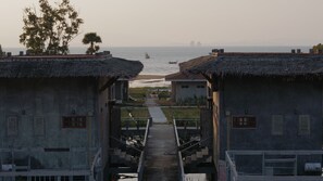 Un camino que lleva a una playa con edificios de techo de paja y vistas al mar.