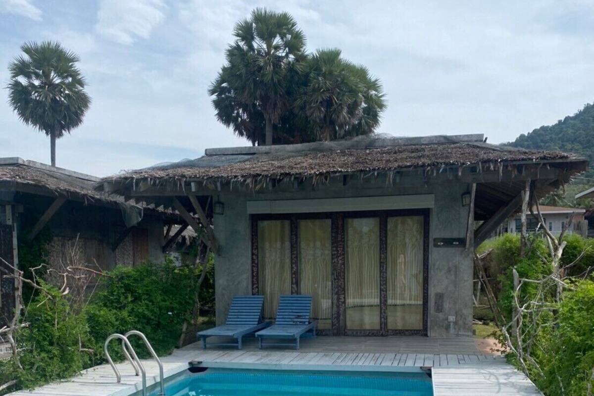 Una piscina con muelle de madera, dos sillas de descanso y un pequeño edificio con techo de paja.