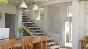 Un intérieur rustique avec un escalier en bois, une table à manger entourée de chaises et des luminaires suspendus.