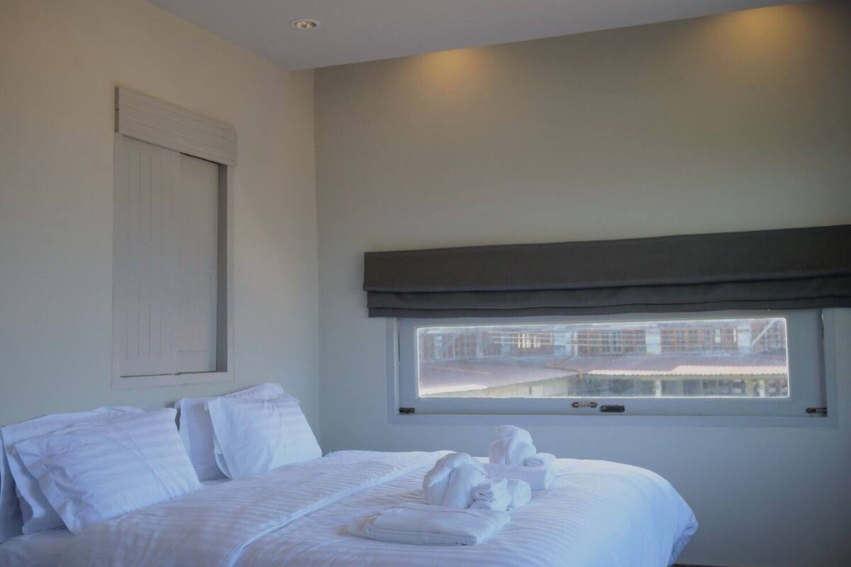 Una habitación de hotel con una cama grande, un ventanal con vistas a edificios y una persiana de color oscuro.