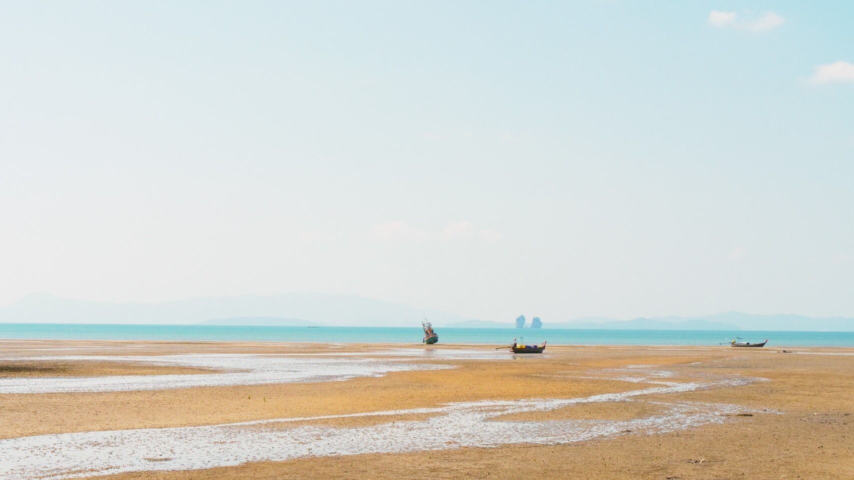 Una playa con barcos y una formación rocosa a lo lejos.