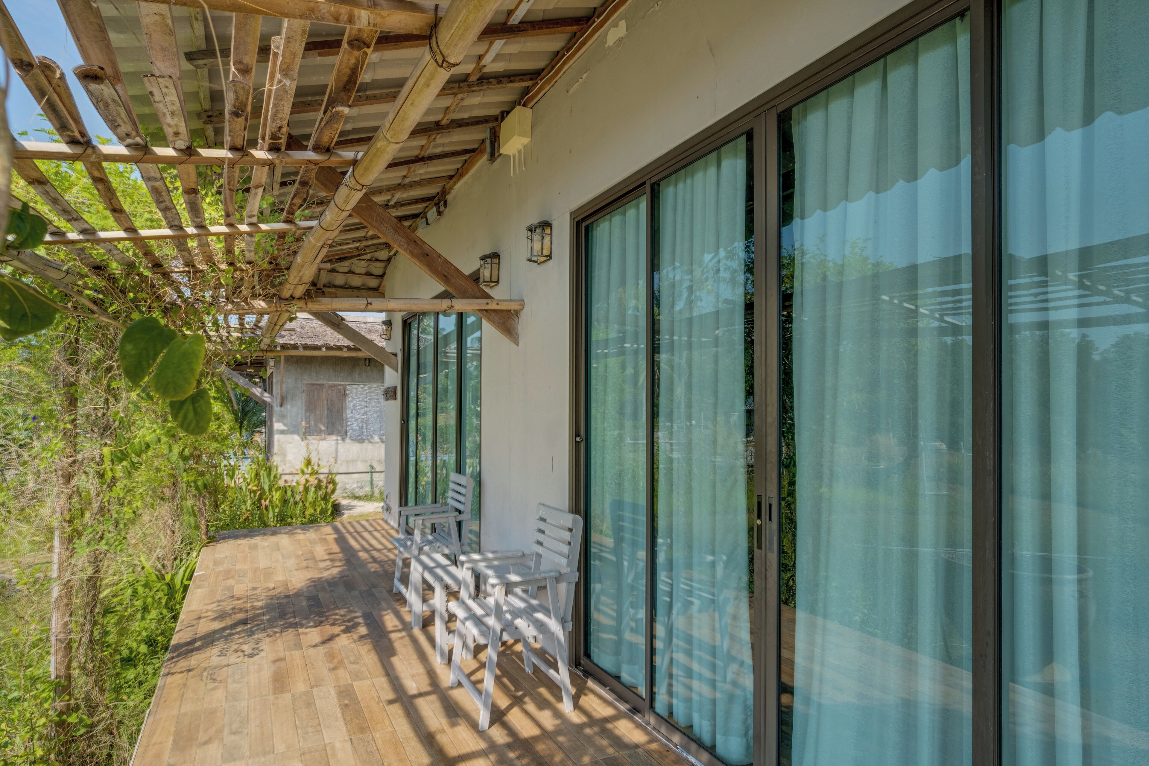 Un'area relax esterna riparata, con pavimento in legno, sedie bianche e ampie vetrate che danno su un edificio.