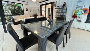 A dining area with a glass-top table, black wicker chairs, a ceiling fan, and a view of the outdoors.