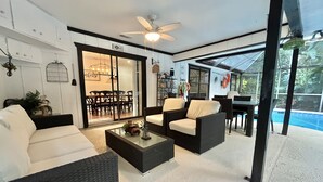 A modern living room with a glass door leading to a dining area, a ceiling fan, and a pool visible through the glass.