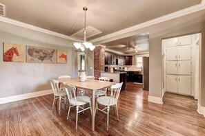 Un comedor con una mesa de madera y sillas blancas, una cocina con armarios oscuros y una puerta blanca.