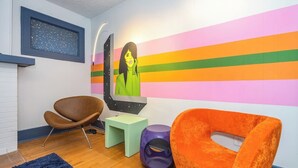 Ein modernes Zimmer mit Holzboden, einem braunen Ledersessel, einem kleinen grünen Tisch, einem violetten Hocker und einem orangefarbenen Sessel.