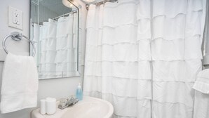 Ein Badezimmer mit weißem Waschbecken, einem Spiegel, einem Handtuchhalter und einer Duschvorhang.