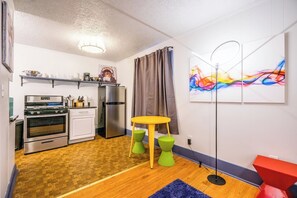 Eine kompakte Küche mit modernen Geräten, ein Essbereich mit kleinem Tisch und Hockern sowie ein farbenfrohes abstraktes Bild an der Wand.