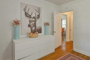 A hallway with a white console table, a deer painting, two vases with dried flowers, and a patterned rug. - Communal Crashpad (Oklahoma City)