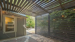 Et overdækket udendørs område med en træpergola, et lille skur og et hegn med slyngplanter.