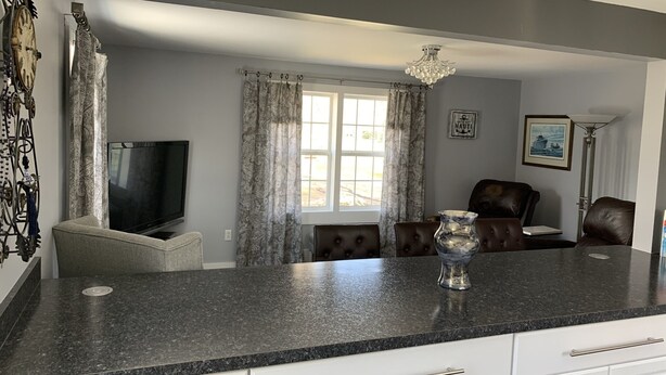 Una cocina moderna con encimera de granito, armarios blancos y una zona de comedor con sillas de cuero.