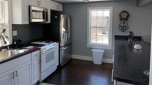 Una cocina moderna con armarios blancos, electrodomésticos de acero inoxidable, encimera negra y una araña.