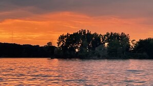 Un atardecer sobre una masa de agua tranquila con una costa arbolada.