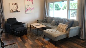 A living room with a sofa, ottoman, and chairs, a coffee table, and artwork on the wall.