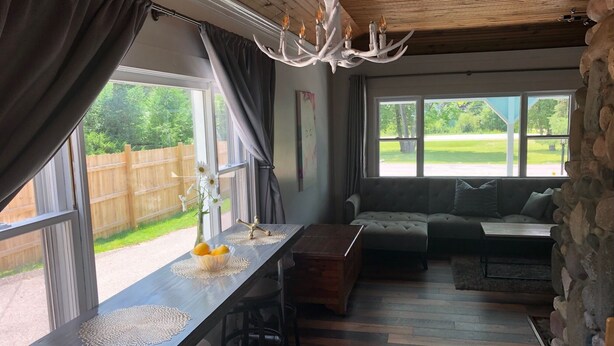 A cozy room with a wooden ceiling, a stone wall, a wooden dining table with a vase of flowers, a sofa, and a chandelier.