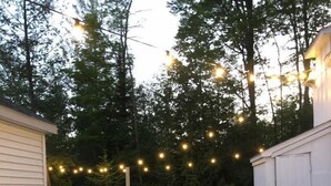 A wooden picnic table with a can of soda, surrounded by a grassy area with trees and string lights.