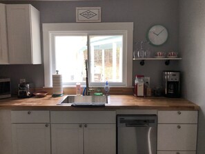A kitchen with a window, a sink, a coffee maker, and a clock on the wall.