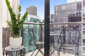 A balcony with a potted plant, a small round table, and two chairs.