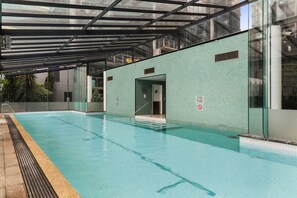 A swimming pool with a glass enclosure, a tiled wall, and a door leading to an indoor area. - Luxe 2-Bed Apartment with River Views Near Casino (Southbank)
