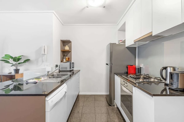 Eine kleine Küche mit Geschirrspüler, Spüle, Herd und Kühlschrank.