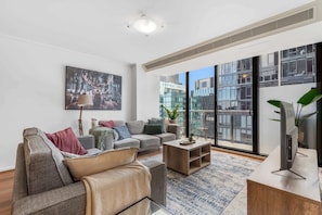 Ein modernes Wohnzimmer mit einer Sofagarnitur, einem Couchtisch und einem großen Fenster mit Blick auf die Stadt.