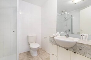 A modern bathroom with a white toilet, a marble sink, and a large mirror.