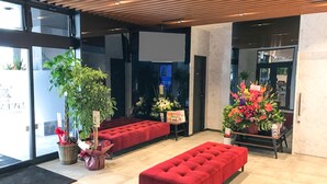 A modern lobby with a red bench, potted plants, and a large window. - Hotel Livemax Fukushima Koriyama Ekimae (Koriyama)