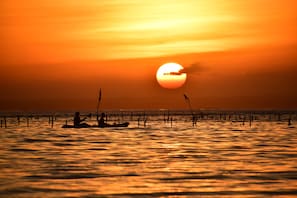 A sunset over a calm sea with a boat and poles in the foreground.