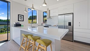 Une cuisine moderne dotée d’un grand îlot central, de tabourets de bar, d’appareils électroménagers en acier inoxydable et offrant une vue sur l’extérieur.